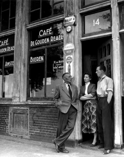 Jan Mens in 1959 voor café De Gouden Reael op de Zandhoek, in gesprek met kroegbaas Hein de Boer en diens vrouw. In zijn populaire roman De Gouden Reael(1940) beschreef Mens het buurtleven rond dit café omstreeks 1900. (Foto: Henk Nieuwenhuys/Spaarbestad Fotoarchief).
